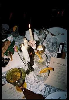 a table topped with plates and glasses filled with food next to candlelight candles on top of paper napkins