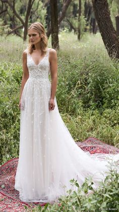 a woman in a white wedding dress standing on a red and blue rug with trees behind her