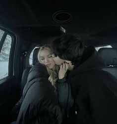 two people kissing in the back seat of a car on a snowy day at night