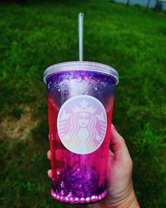 a hand holding up a pink and purple starbucks cup with glitter on the outside,