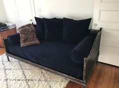 a blue couch with pillows on top of it in front of a white wall and wooden floor