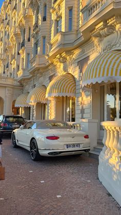 a white car parked in front of a building with yellow and white awnings