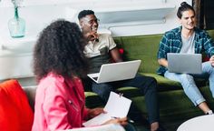 three people sitting on a couch with laptops