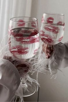 two wine glasses with red lipstick painted on them are being held by someone's hands