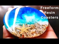 a hand holding a blue and white rock with a starfish on it that reads, freeform resin coasters