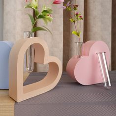 two vases with flowers in them on a table next to a heart shaped object