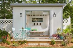 a small white shed sitting in the middle of a yard with a table and chairs