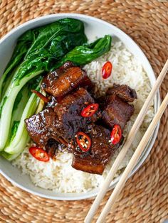 a white bowl filled with meat and vegetables next to chopsticks on top of rice