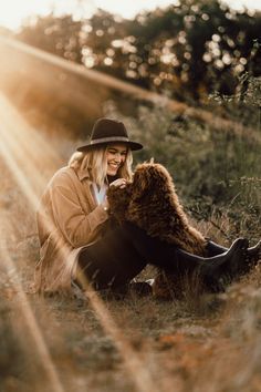 a woman sitting on the ground with a bear in her lap and wearing a hat