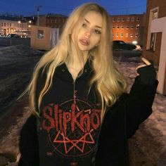 a woman with long blonde hair wearing a black shirt and standing in front of a building