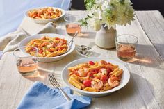 two plates of pasta with shrimp and tomatoes on a table next to glasses of water