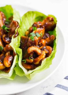 two lettuce wraps filled with meat and sauce on a plate next to a fork