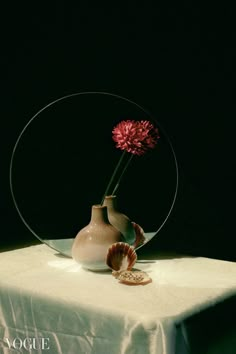 a vase with a flower in it sitting on a table next to a seashell