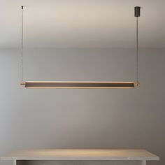 a long light fixture hanging from the ceiling over a table with a bench underneath it