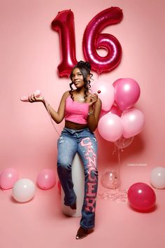 a woman in pink shirt and jeans standing next to balloons with the number sixteen on it