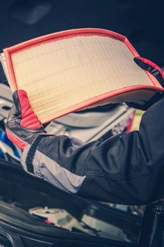 a close up of a person holding an air filter in front of a car trunk