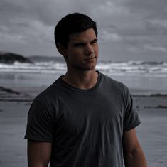 a man standing in front of the ocean on a cloudy day with his eyes closed