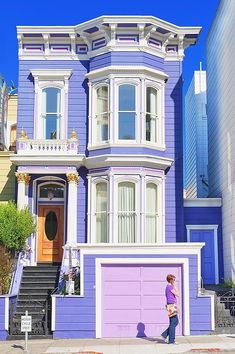 a woman walking down the street in front of a purple house with two storys