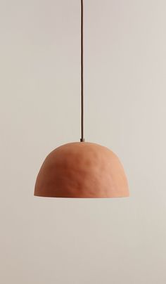 a brown light hanging from a ceiling with a white wall in the background and an orange lamp shade