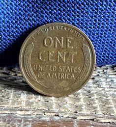 an old one cent coin sitting on top of a piece of wood next to a blue cloth