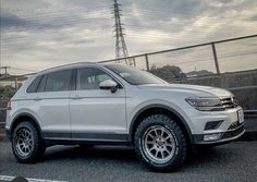 a white volkswagen suv parked in front of a chain link fence on a cloudy day