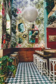 the interior of a restaurant with colorful wallpaper and checkered flooring, potted plants