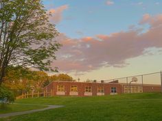 a school building sitting on the side of a lush green field next to a tree