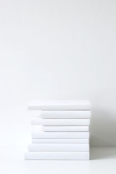 a stack of white sheets sitting next to each other on top of a table in front of a white wall