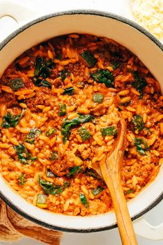 a pot filled with pasta and spinach on top of a white table next to a wooden spoon