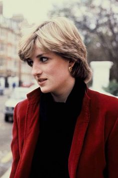 a woman in a red jacket and black shirt is looking off into the distance with her hand on her hip