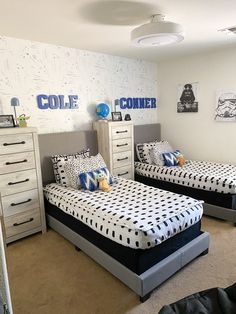 two twin beds in a room with white walls and black and blue decor on the wall