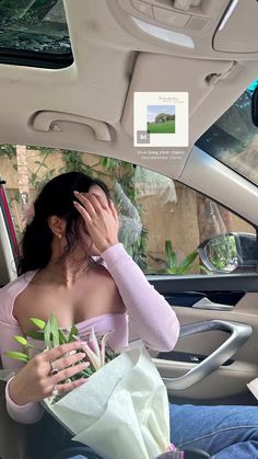 a woman sitting in the back seat of a car holding flowers and looking at her cell phone