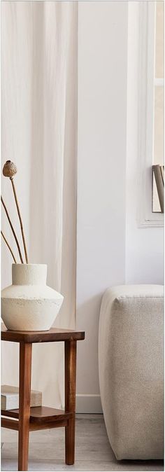 a white vase sitting on top of a wooden table next to a chair and window