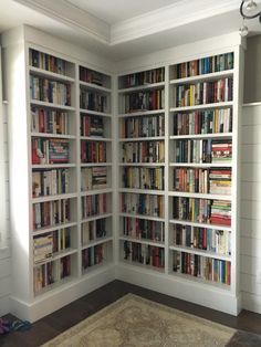 a living room filled with lots of books on top of white bookcases next to a rug