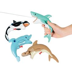 a hand is holding three toy sharks and one shark has a toothpick in it's mouth