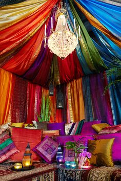 a bed covered in lots of different colored sheets and pillows next to a chandelier