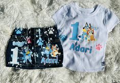 two children's clothing items are laying on a white furnishing surface, one is blue and the other has an image of a dog