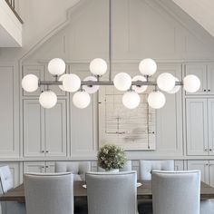 a dining room table and chairs with lights hanging from the ceiling above it in front of white cabinets