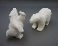 two white ceramic bears sitting next to each other on a gray surface with black background