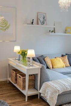 a living room filled with furniture and a white table topped with yellow flowers next to a gray couch