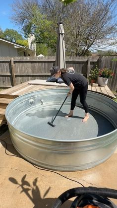 a woman in black shirt and hat cleaning an outdoor swimming pool with a mop