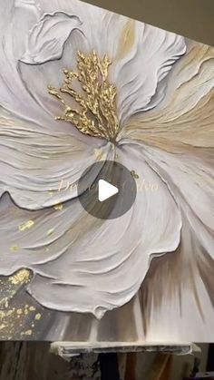 a large white flower is being painted on a canvas with gold leafy details and glitters