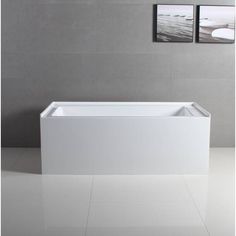 a white bath tub sitting on top of a tiled floor next to two framed pictures