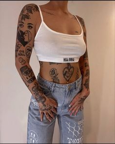 a woman with tattoos on her arms and chest standing in front of a white wall