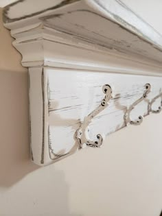 an old white painted shelf with decorative brackets on the top and bottom, hanging from a wall