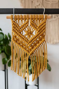 a yellow macrame hanging from a wooden pole next to a potted plant