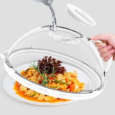 a person is pouring water into a bowl filled with pasta and veggies on a white plate