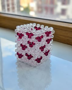 a red and white beaded bracelet sitting on top of a table next to a window