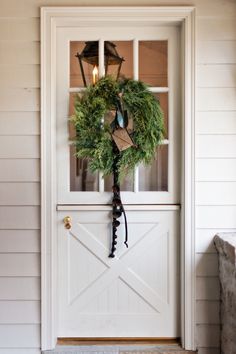 a wreath hanging on the front door of a house with two lights and a lantern