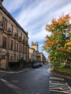 an empty street with cars parked on the side and trees lining the road in autumn